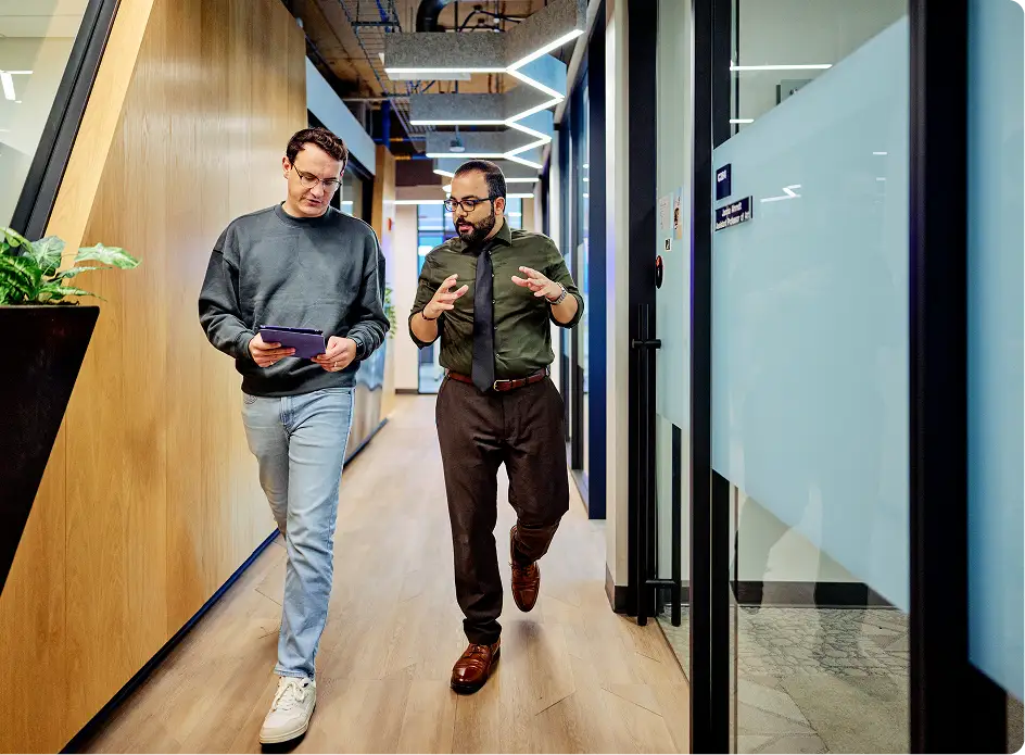 two men walking down hall discussing while looking at a tablet